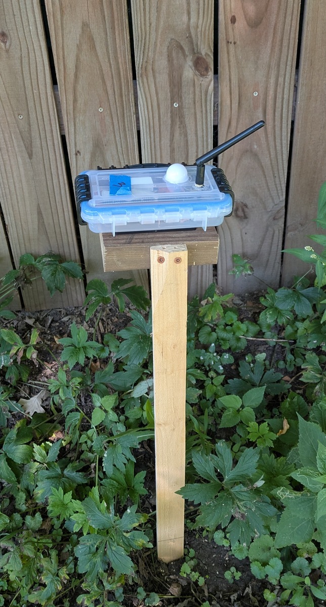 The complete sensor prototype in its enclosure, mounted on a wooden stake stand.
